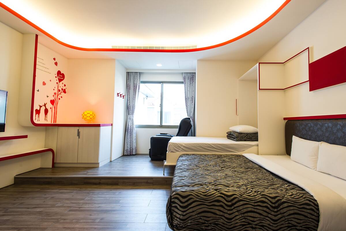 Habitació d'hotel moderna amb llit, escriptori, cadira i una petita finestra amb cortines.