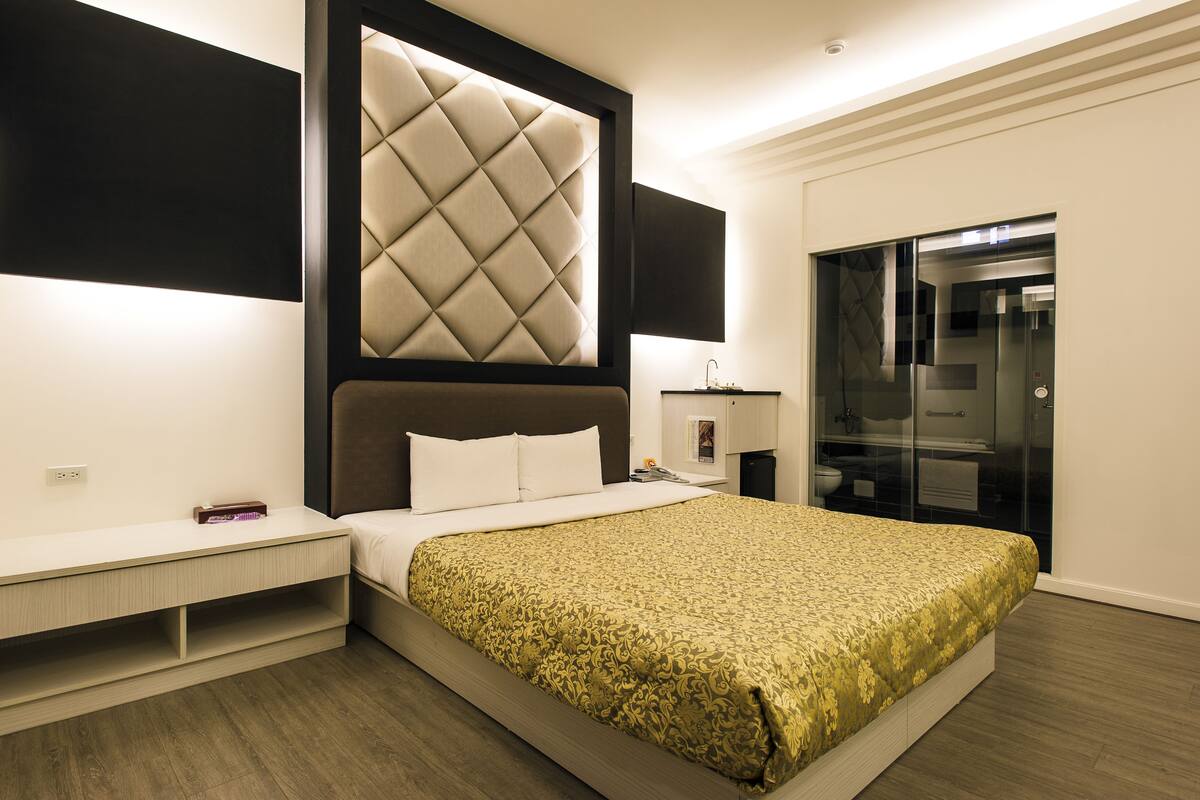 Habitació d'hotel moderna amb un llit gran, televisió integrada, taula de nit i dutxa amb envà.