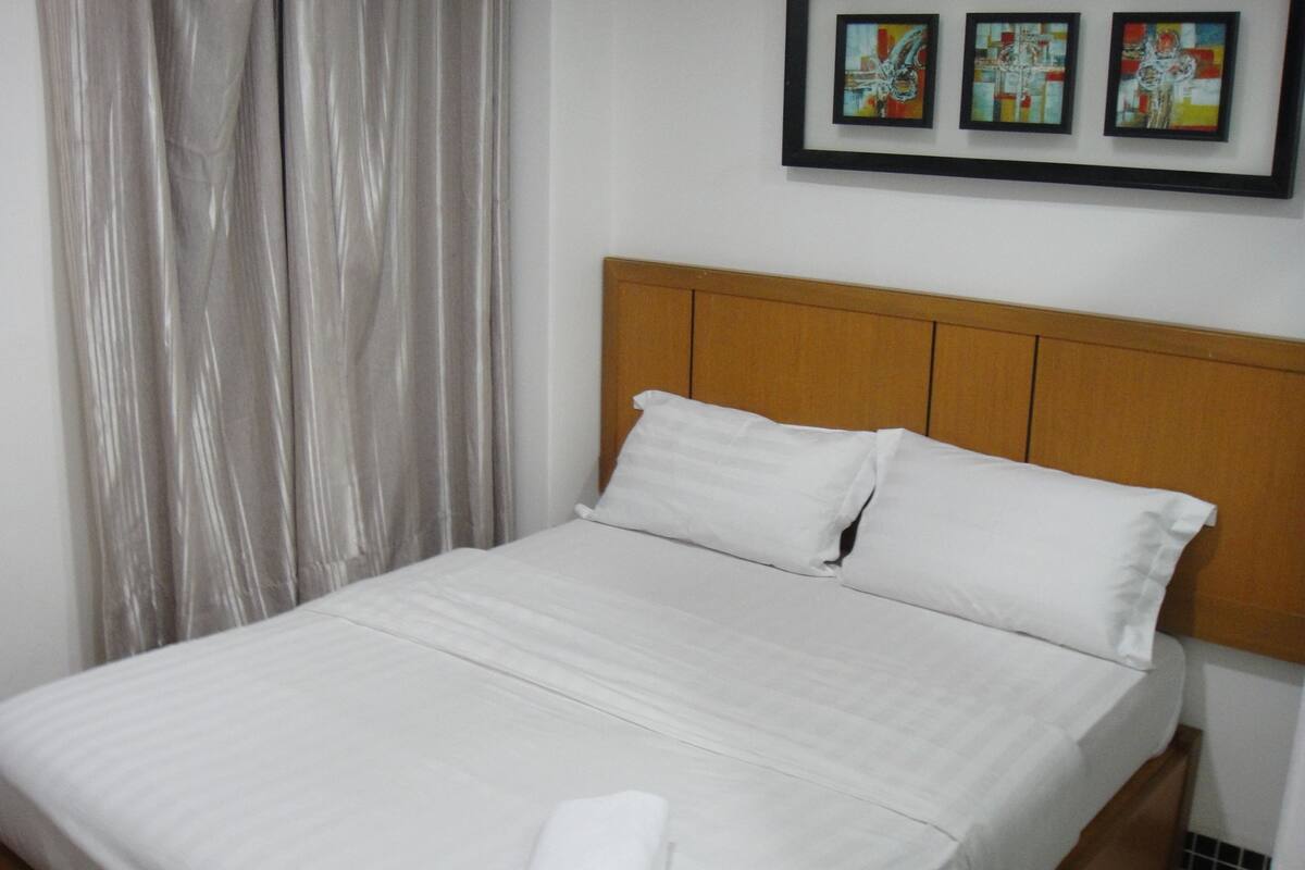 A neatly made bed with white linens and pillows, a wooden headboard, and a small folded towel on the bed.