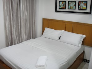 Una cama bien hecha con sábanas y almohadas blancas, cabecera de madera y una toalla doblada sobre la cama.