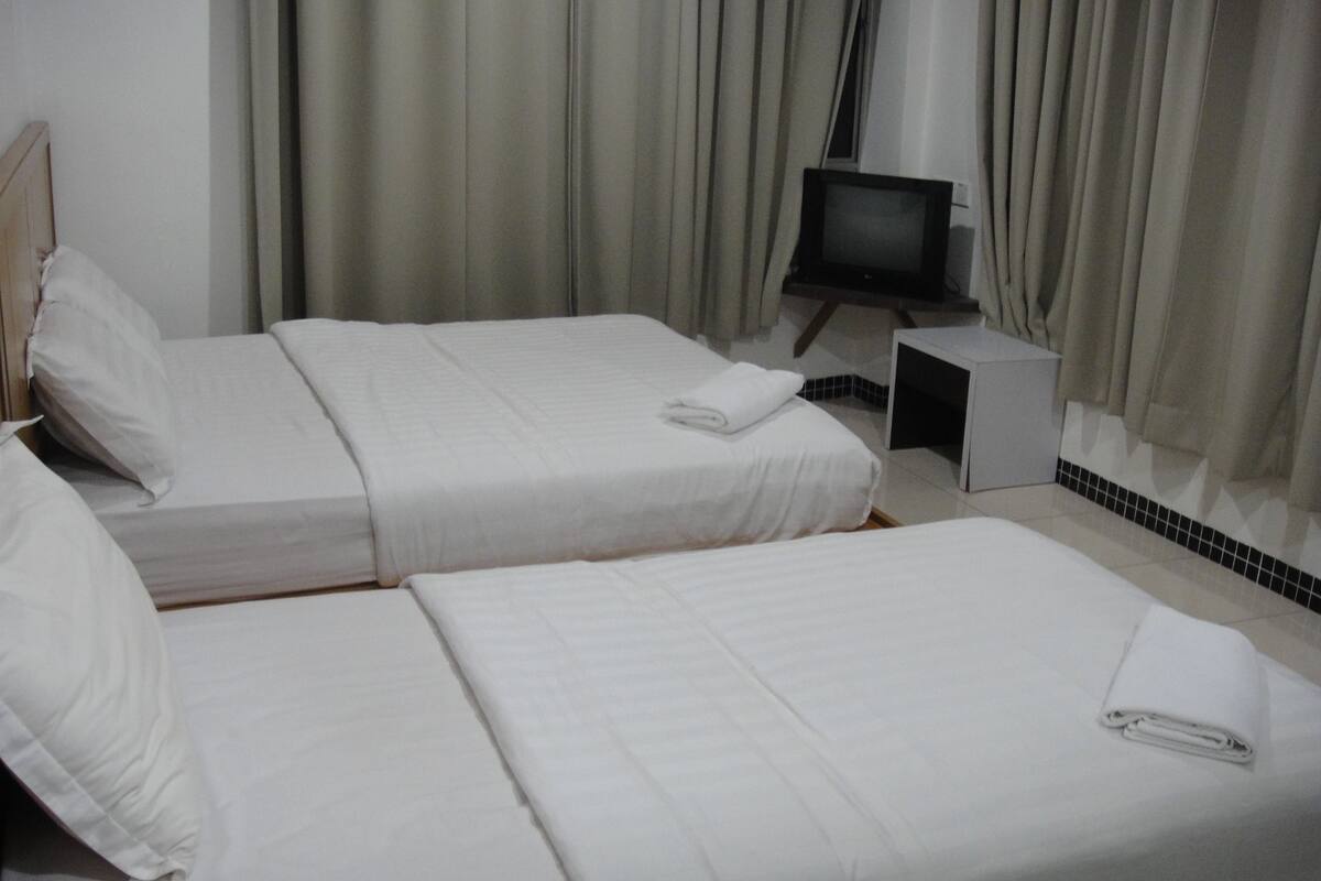 A hotel room with two beds, a TV on a stand, and curtains.