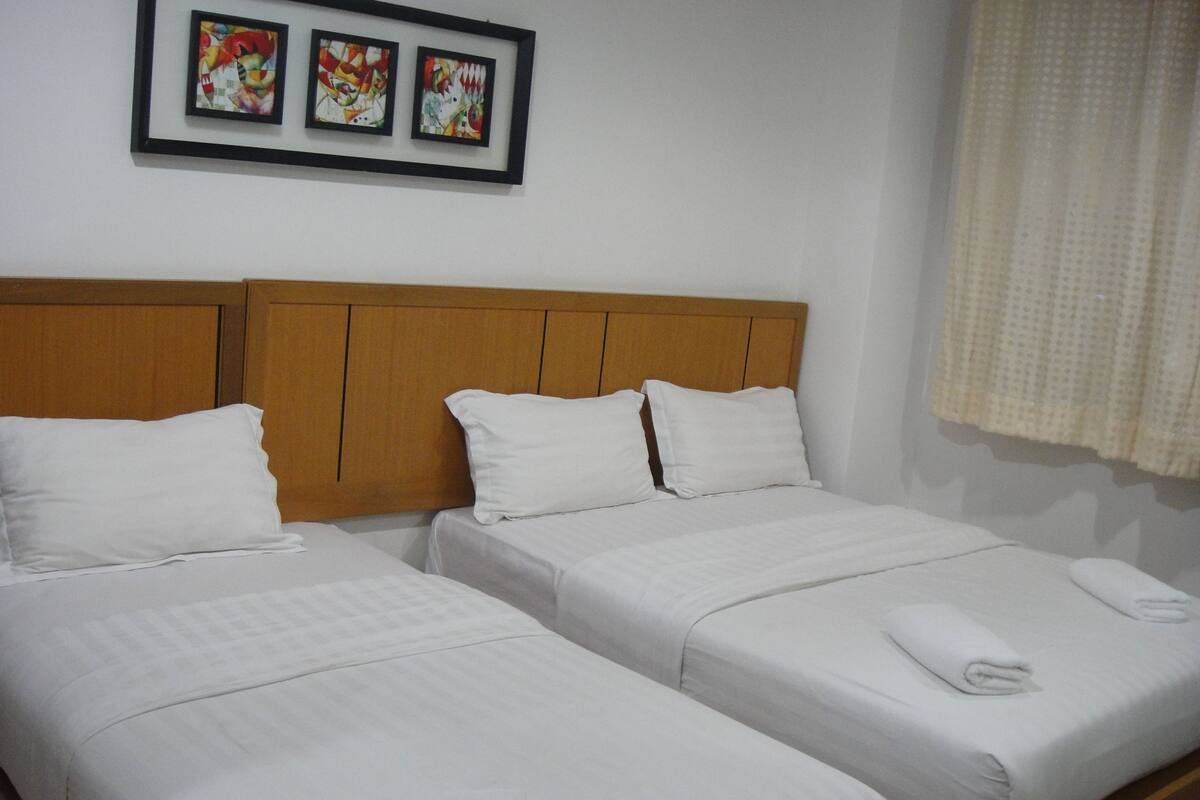 A hotel room with two single beds, a wooden headboard, white bedding, and two framed artworks on the wall.