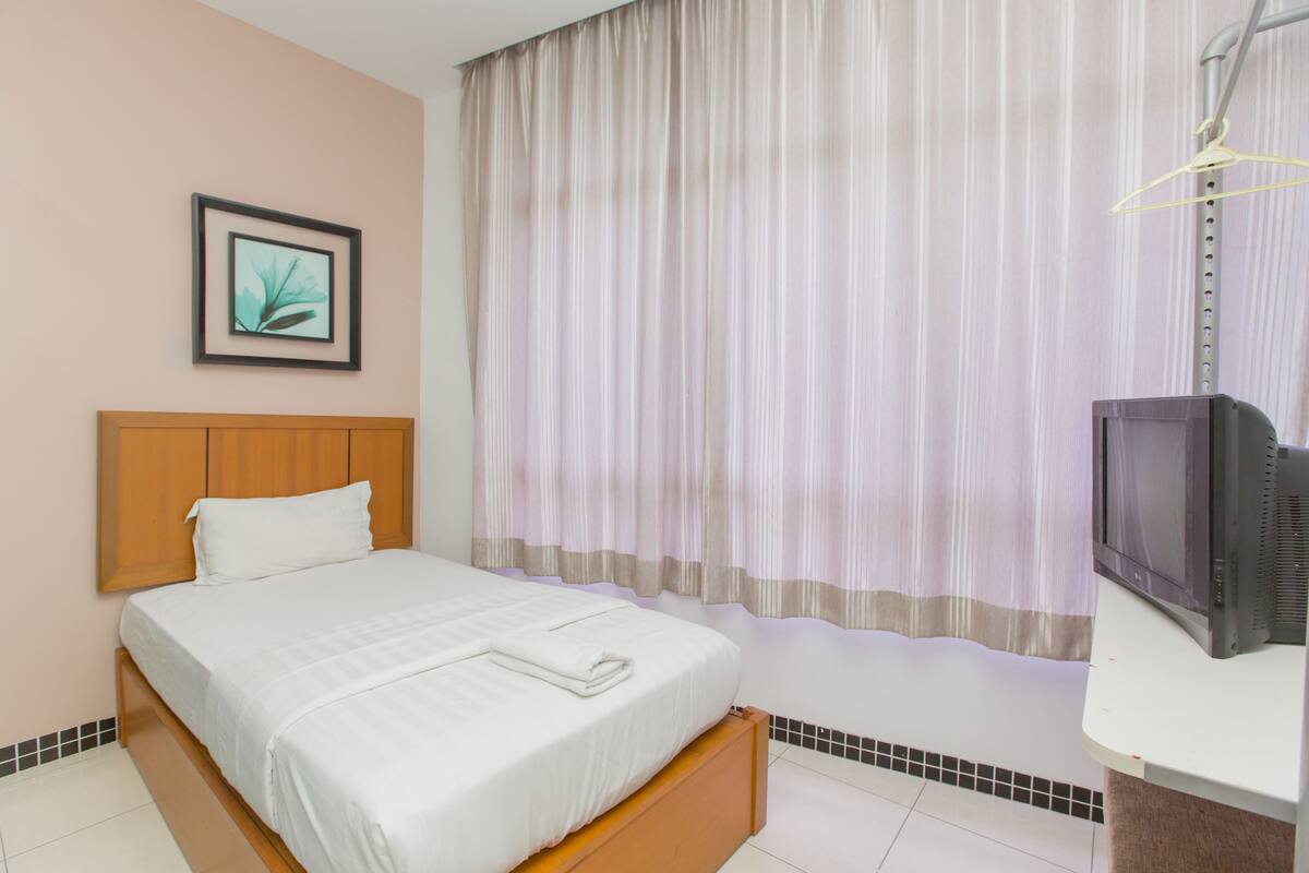 A hotel room with a bed, a television, a framed picture on the wall, and a window with curtains.