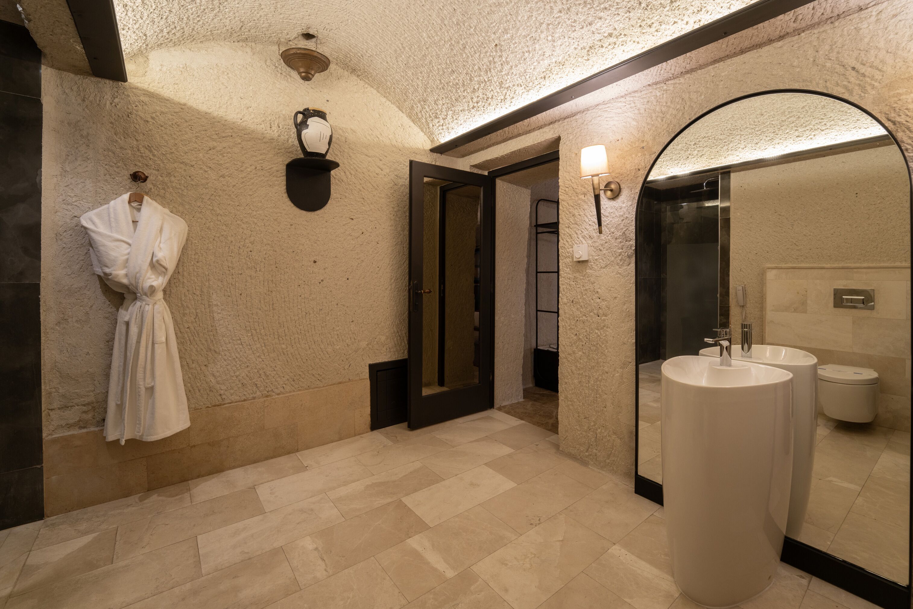 Un baño moderno con un espejo grande, dos lavamanos y una bata colgada en la pared.