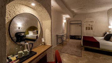 Een knus hotelkamer met een ronde spiegel, een houten bureau met een koffiezetapparaat, een bed met een rode deken en een klein tafeltje met een stoel.