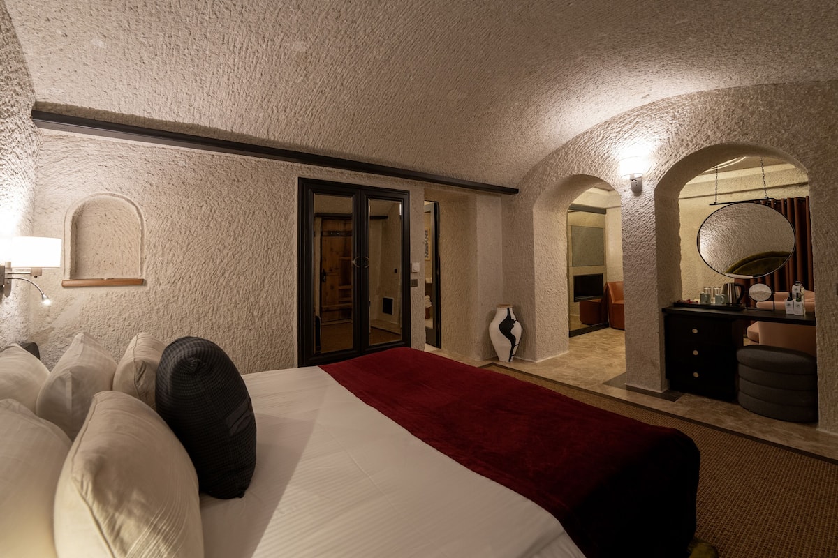 Camera d'albergo con un letto grande, una coperta rossa, uno specchio, un comò e una porta che dà sul bagno.
