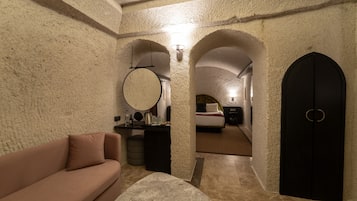 Quarto com parede de pedra, espelho redondo, sofá, cama e porta preta.