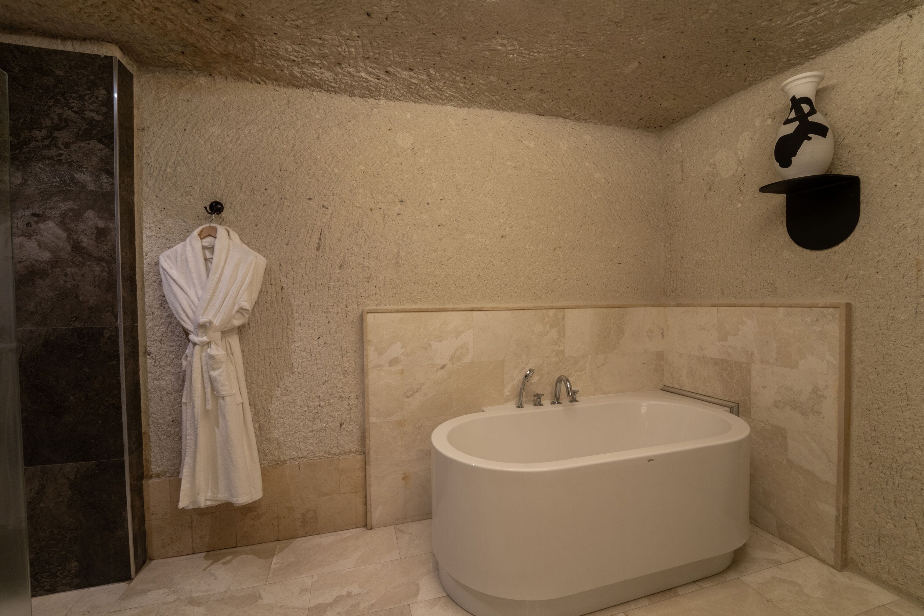 Een moderne badkamer met een vrijstaand bad, een badjas hangend aan de muur en een handdoekrek.