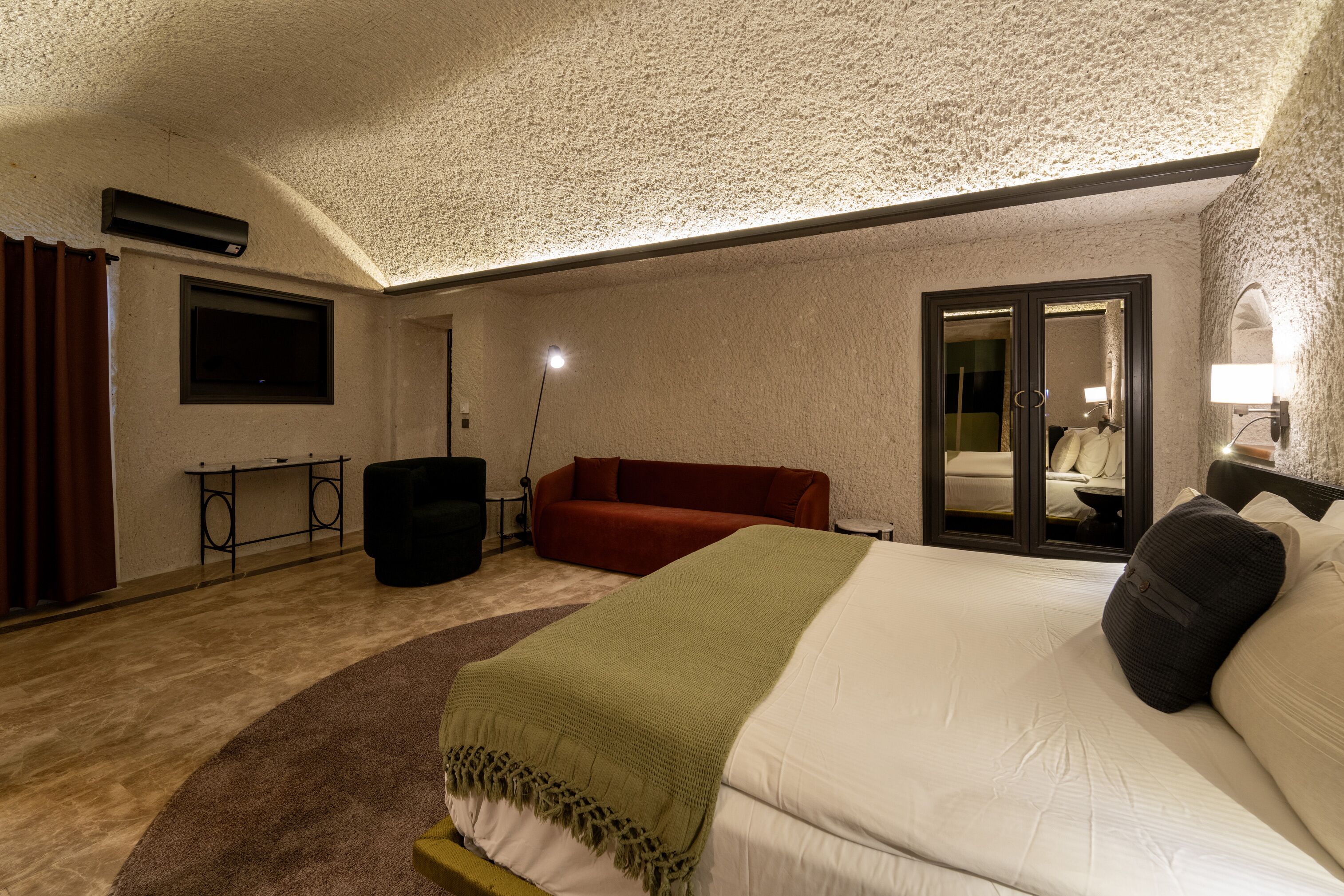 Quarto de hotel com uma cama grande, um sofá vermelho, um espelho e uma pequena mesa.