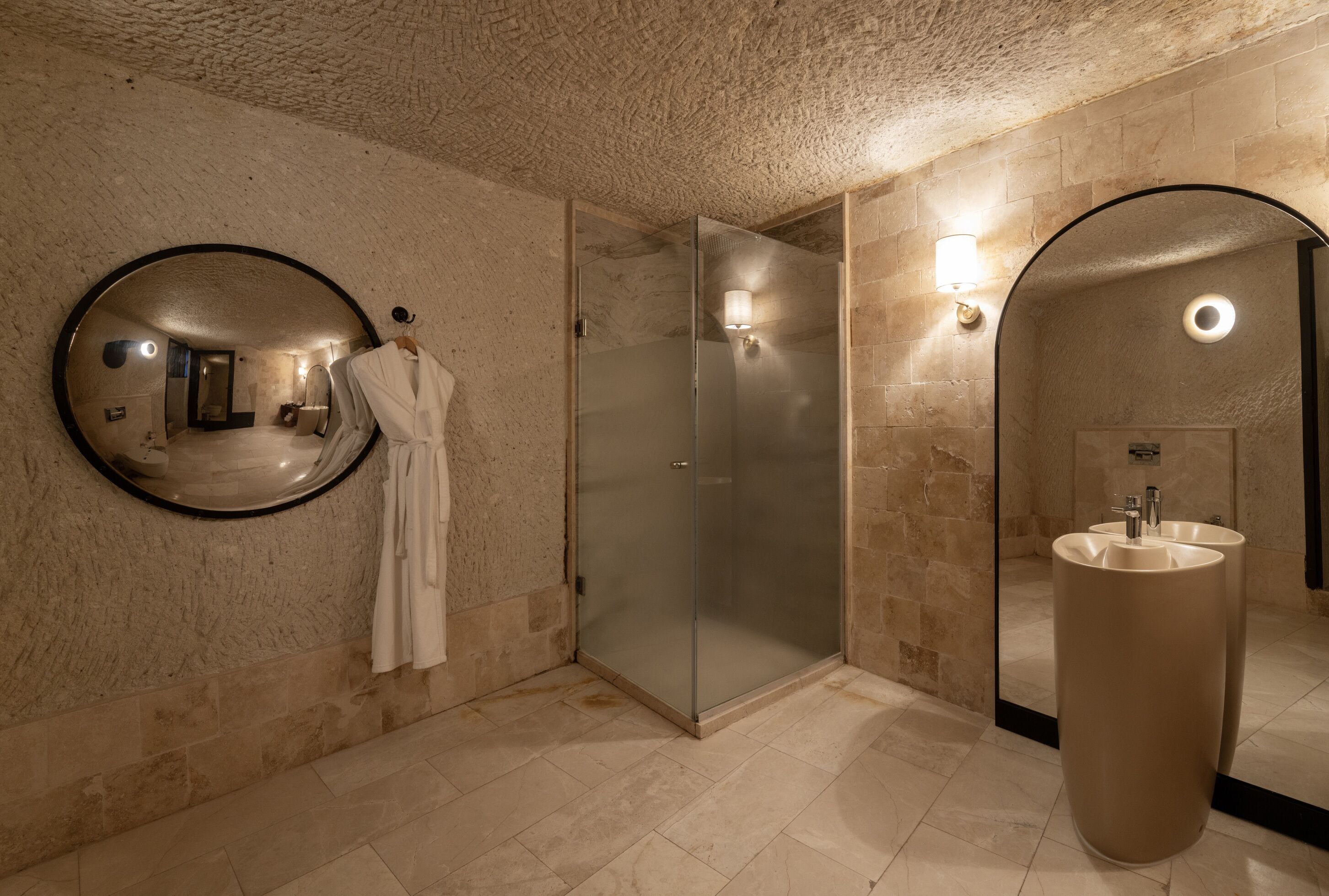 Un baño moderno con un espejo redondo, una ducha con cerramiento de vidrio y un lavamanos grande.