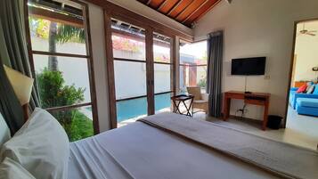 Quarto com cama, escrivaninha, cadeira, TV e vista para piscina e jardim.