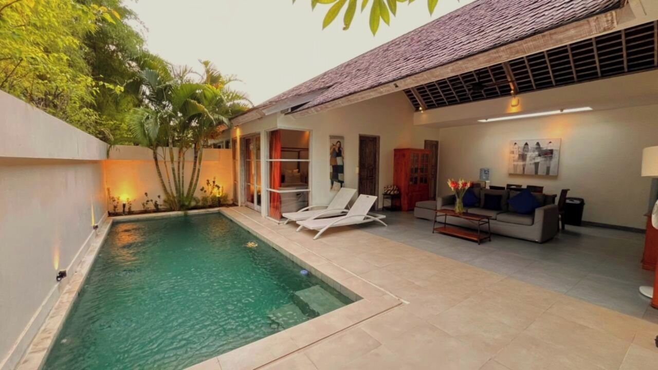 Un área moderna junto a la piscina con piscina, sillas de descanso y un espacio de estar con sofá y mesa.
