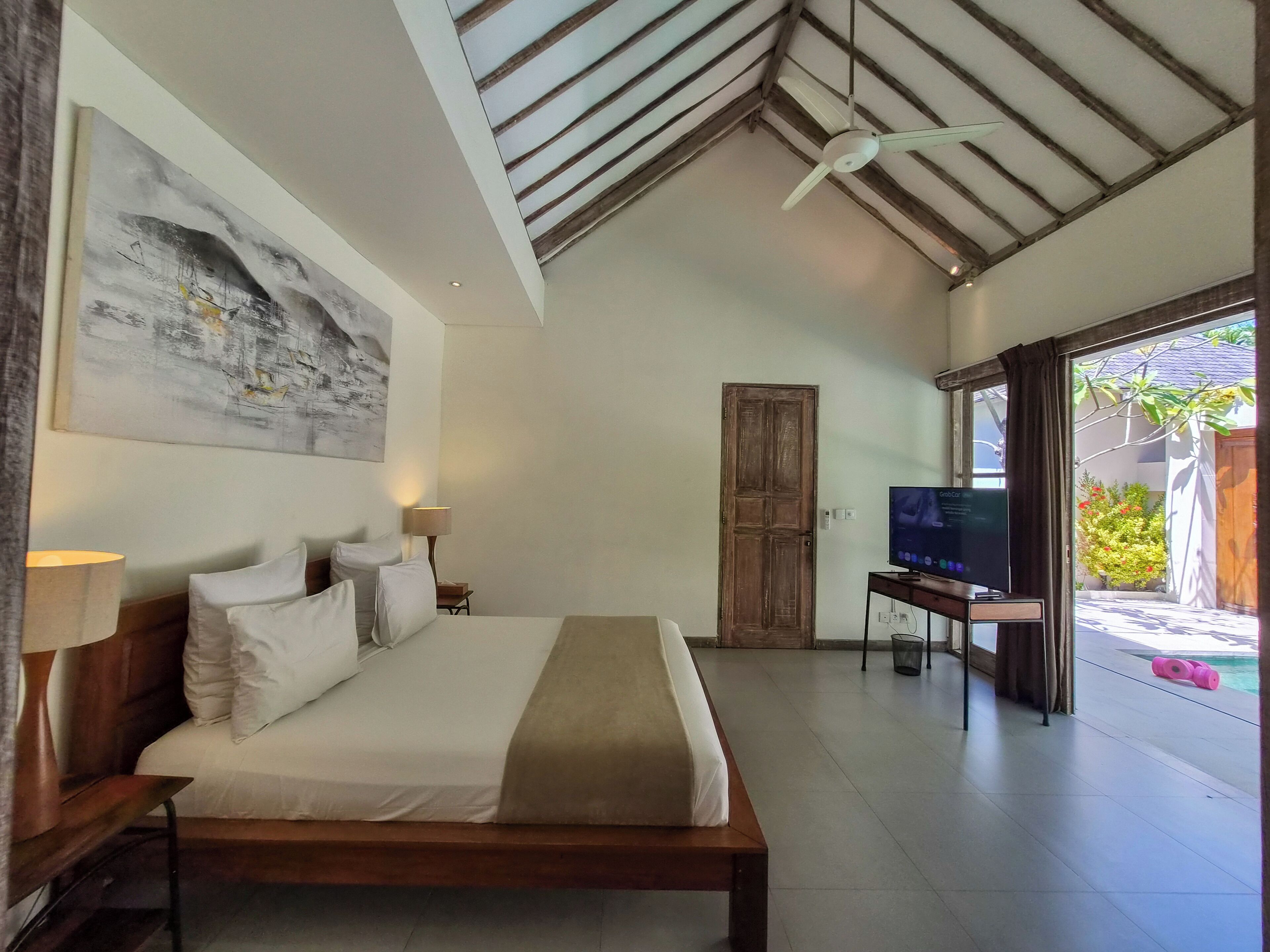A bedroom with a bed, a television, and a ceiling fan.