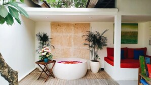 A modern interior with a round seating area, a wooden table with a vase of flowers, and a red couch. - The Decks Bali (Legian)