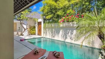 Zona de piscina con sillones de descanso y vista a un jardín con bambú y plantas en flor.