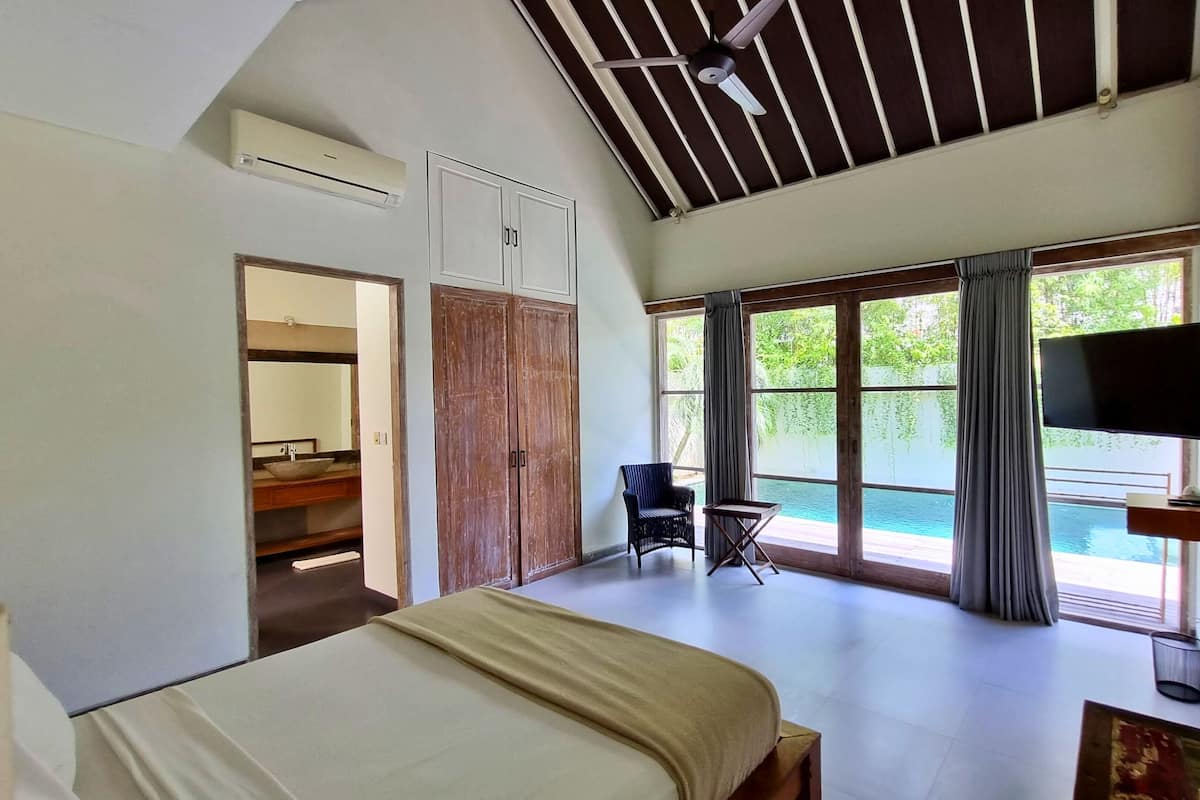 A bedroom with a bed, a chair, a TV, and a view of a pool.