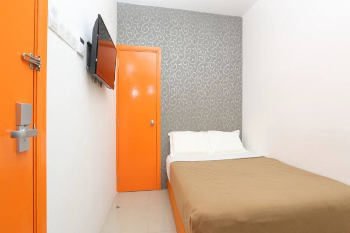 A hotel room with a bed, a television mounted on the wall, and an orange door.