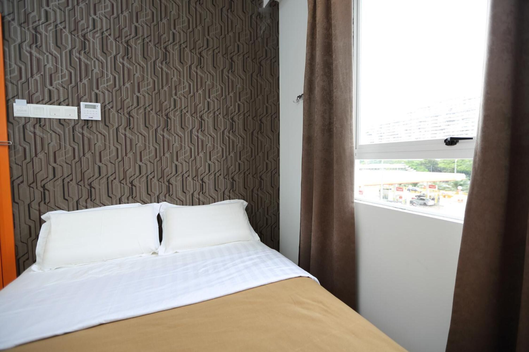 A hotel room with a bed, a patterned wall, a window with curtains, and a view of the outside.