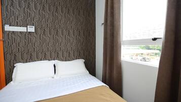 A hotel room with a bed, a patterned wall, a window with curtains, and a view of the outside.