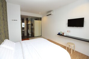 Habitación de hotel moderna con una cama grande, un televisor montado, un taburete pequeño y un baño visible a través de una puerta abierta.