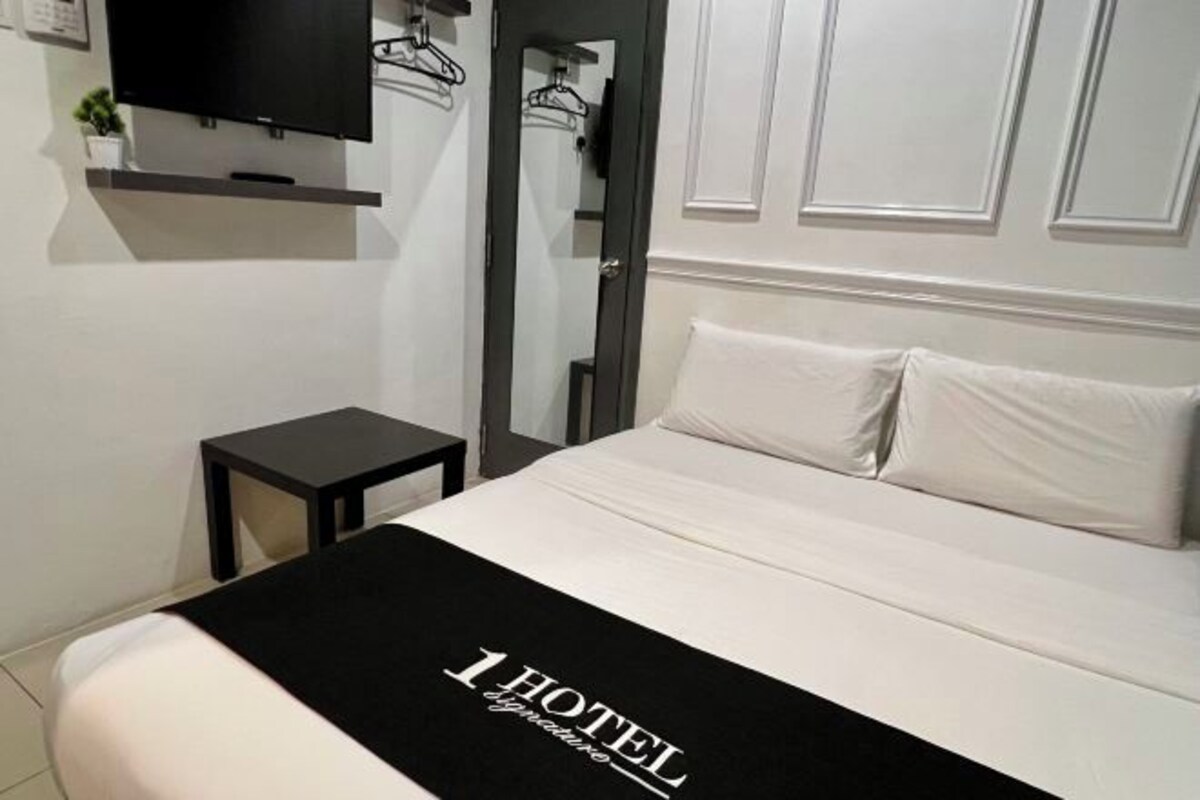 Una habitación de hotel con una cama, una mesita de noche, un televisor montado en la pared y un espejo.