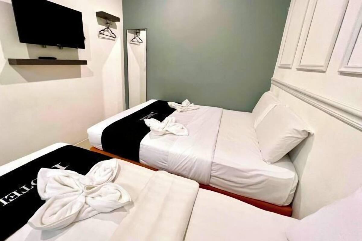 Two single beds with white linens and towels, a flat-screen TV on the wall, and a mirror.