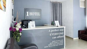 Un mostrador de recepción de hotel con un cartel que dice "1 HOTEL" y una pizarra anunciando estadías económicas.