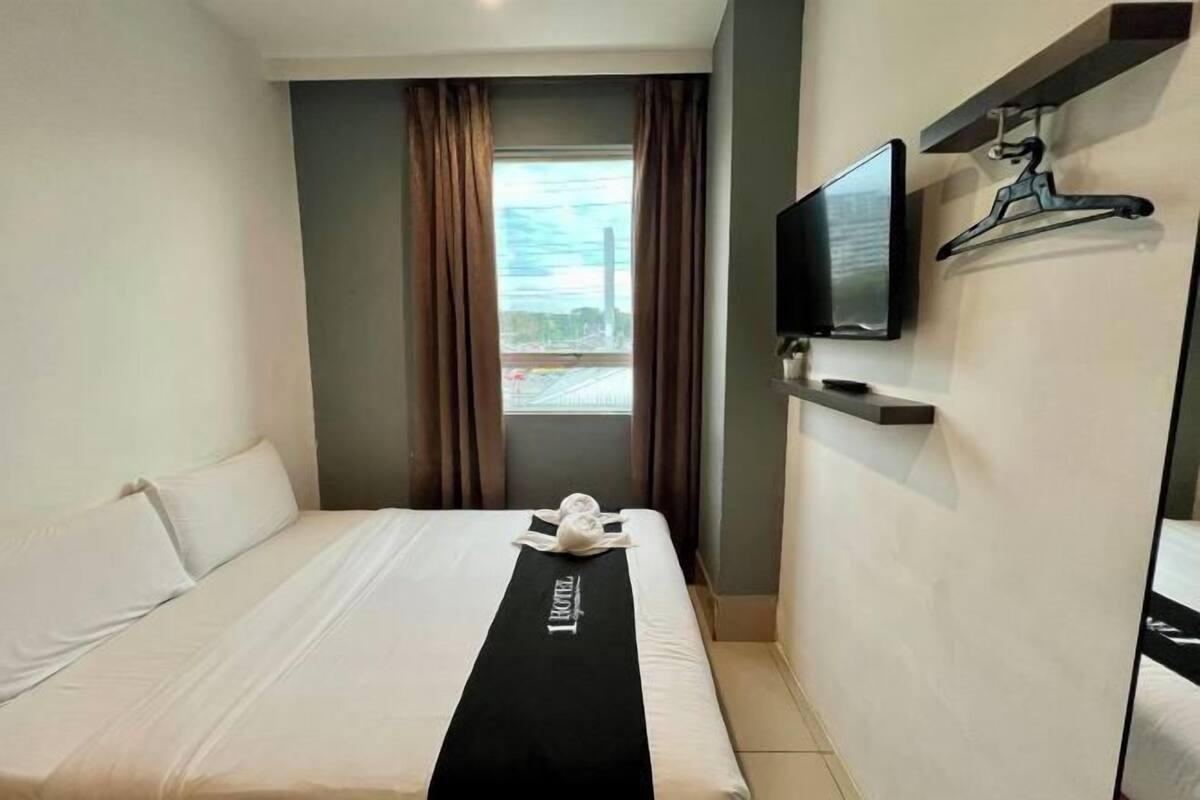 A hotel room with a bed, a flat-screen TV, a window with curtains, and a towel on the bed.
