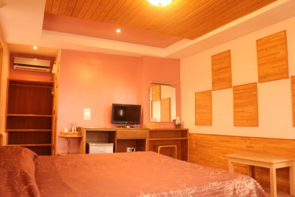 A bedroom with a bed, a desk, a television, a wardrobe, and a mirror.