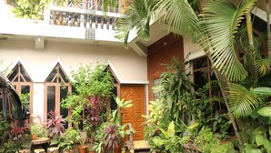 A courtyard with a wooden door, potted plants, and a balcony with railings. - Kaung Lay Inn (Yangon)