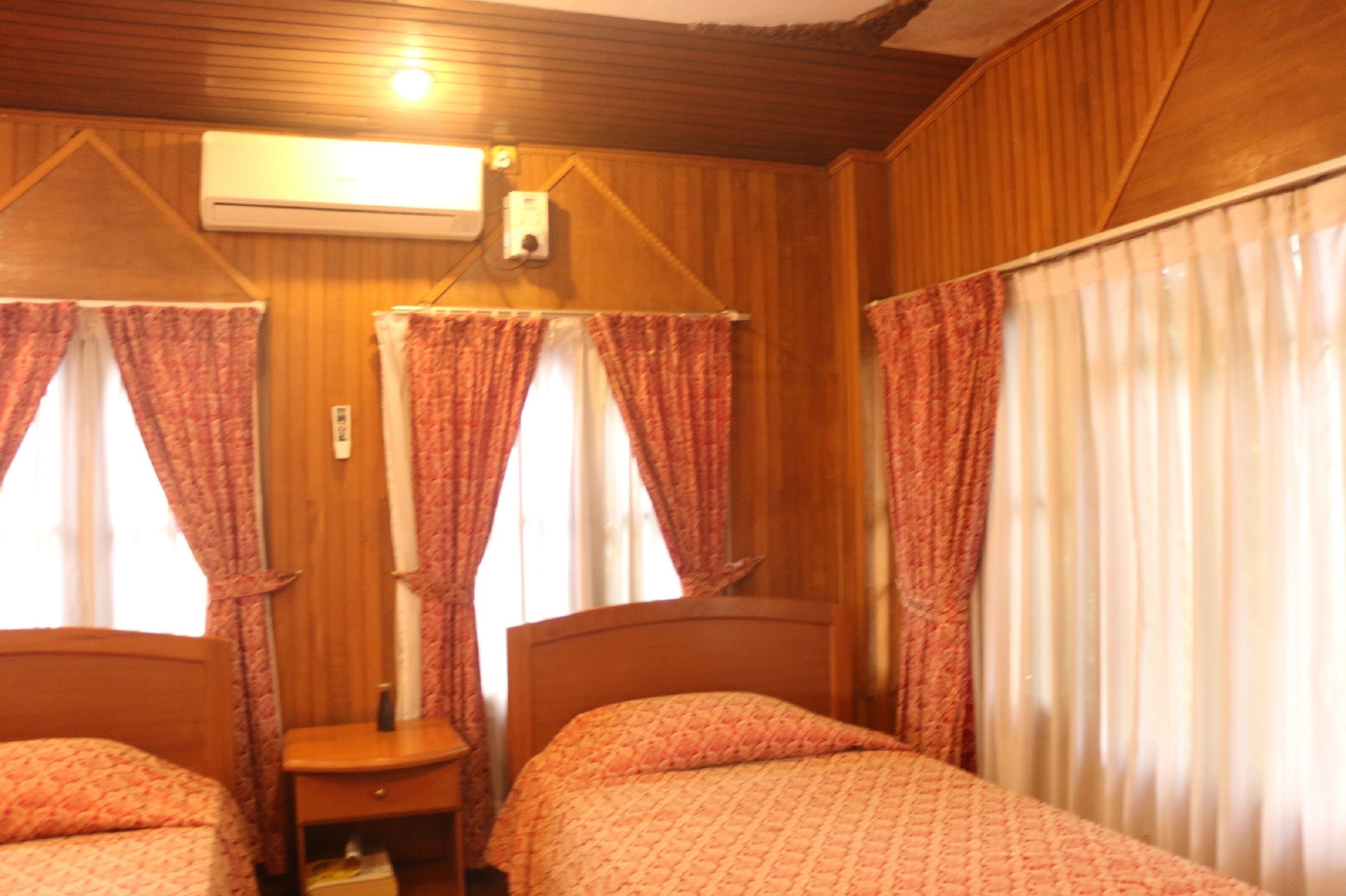 Una habitación con dos camas, paredes de madera, aire acondicionado y cortinas.