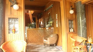 A traditional wooden interior with a checkered floor, wicker chairs, and a counter with decorative items. - Kaung Lay Inn (Yangon)