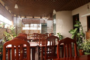 A restaurant with wooden tables and chairs, a lattice partition, and potted plants.