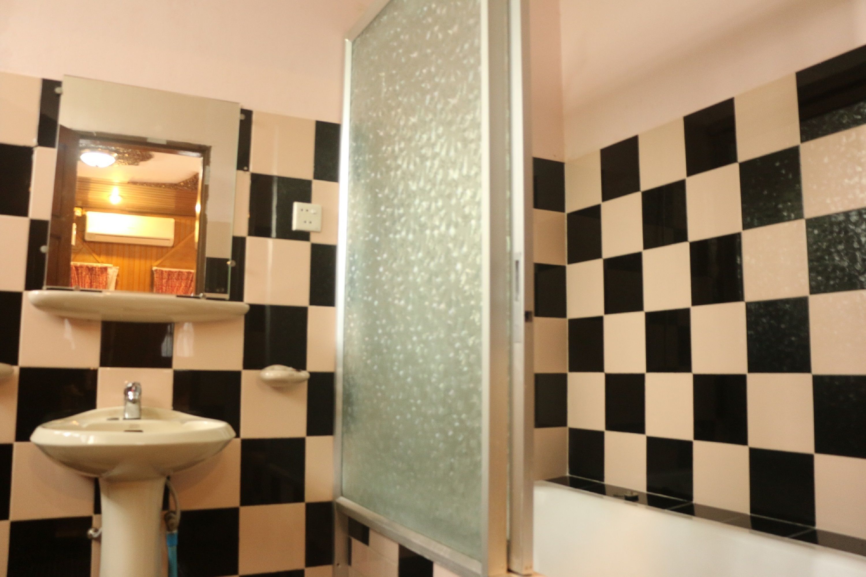A bathroom with a checkered black and white tile wall, a sink, and a mirror.