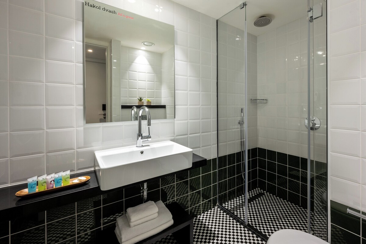 Un baño moderno con un lavamanos blanco, piso a cuadros blanco y negro, y un box de ducha de vidrio.