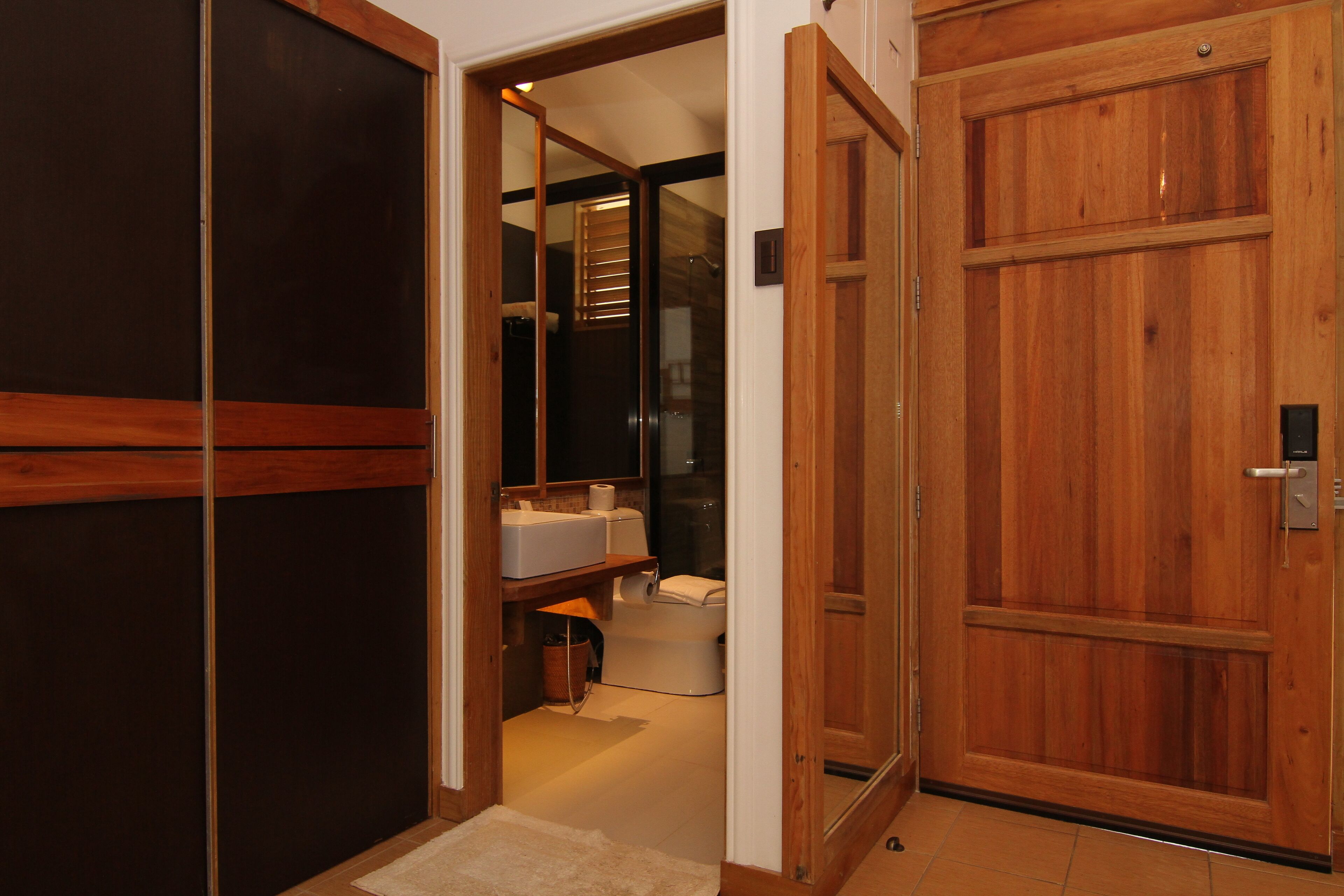 Puerta de madera que da a un baño con inodoro, lavabo y ducha.