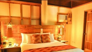 Une chambre à coucher avec une tête de lit en bois, un lit recouvert de draps blancs, deux tables de chevet avec des lampes et une petite fenêtre.