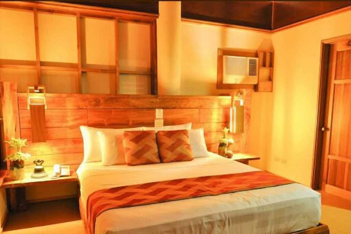 A bedroom with a wooden headboard, a bed with white linens, two bedside tables with lamps, and a small window.