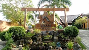 Une enseigne pour Boffo Sand Island, avec une arche en bois, entourée d’un jardin aménagé comprenant diverses plantes et rochers.