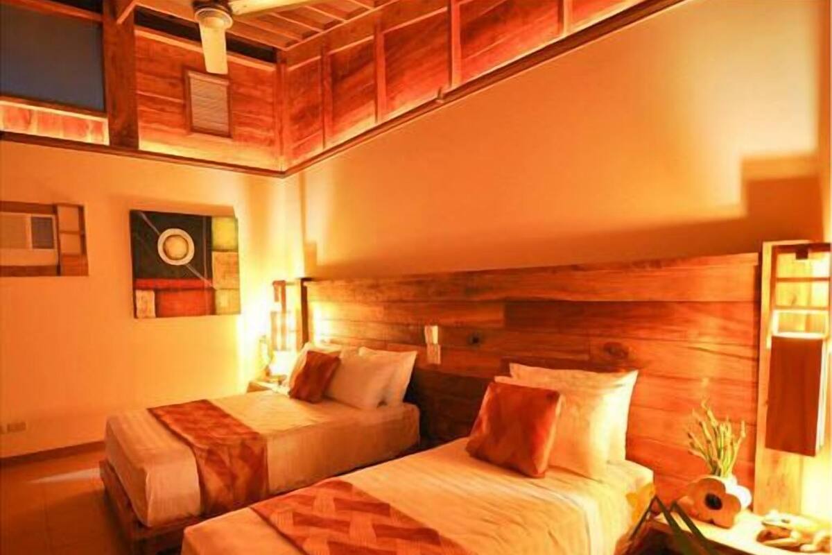 A room with two beds, wooden headboard, and a ceiling fan.