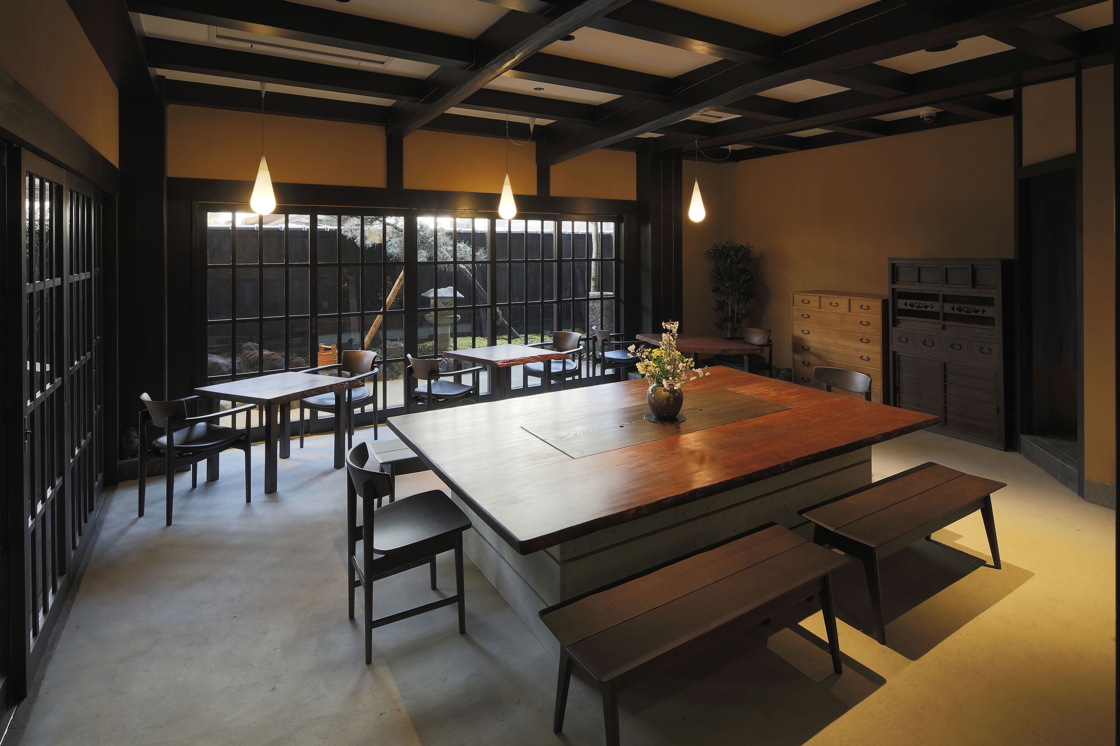 A dining area with a large wooden table, benches, and hanging pendant lights.
