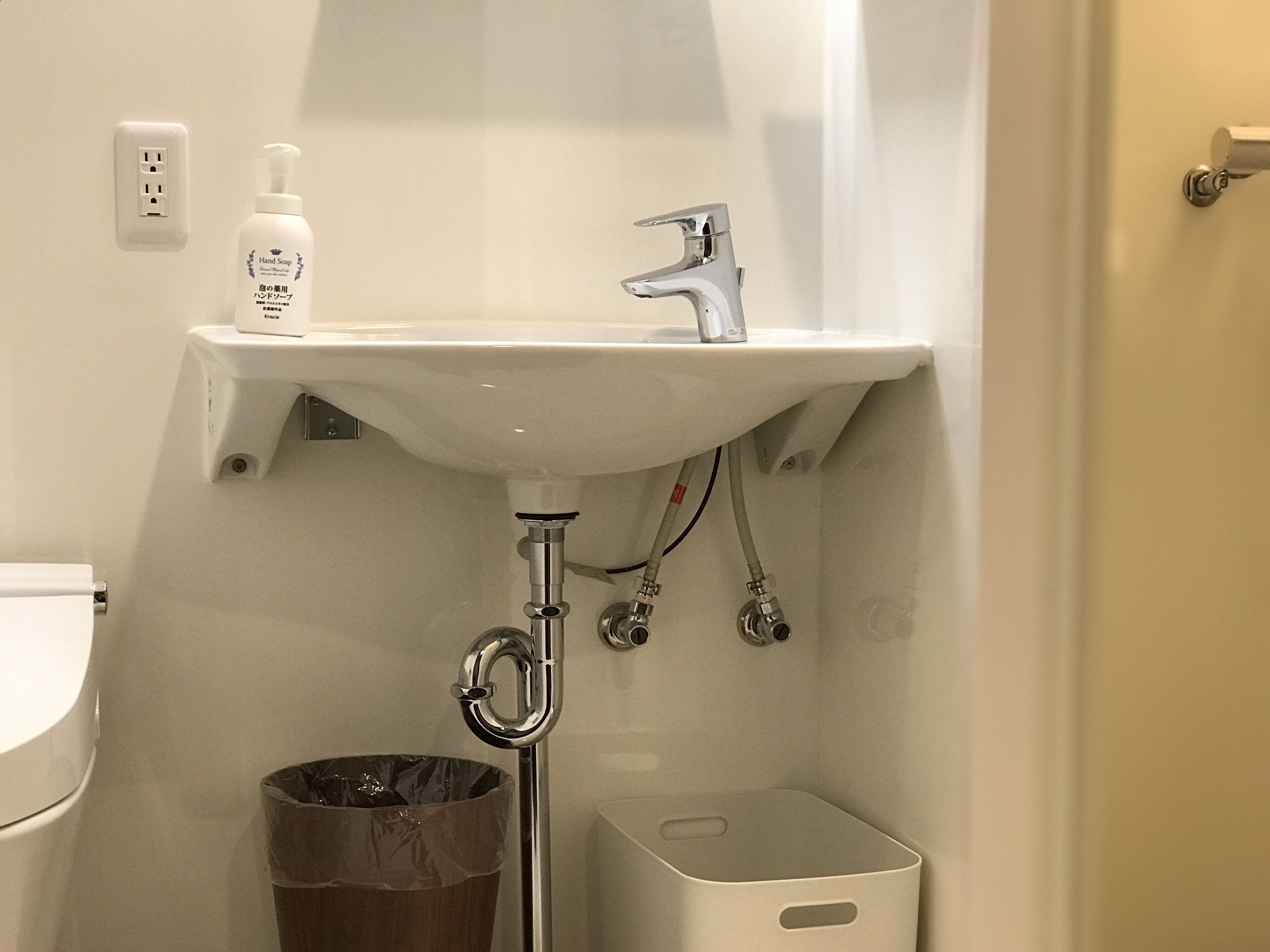 A bathroom with a white sink, a faucet, a hand soap dispenser, a trash can, and a toilet.