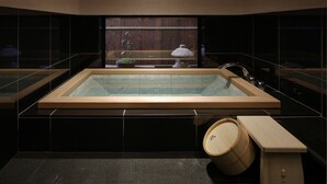 A modern bathroom with a large bathtub, a wooden bench, and a small table with a lamp.