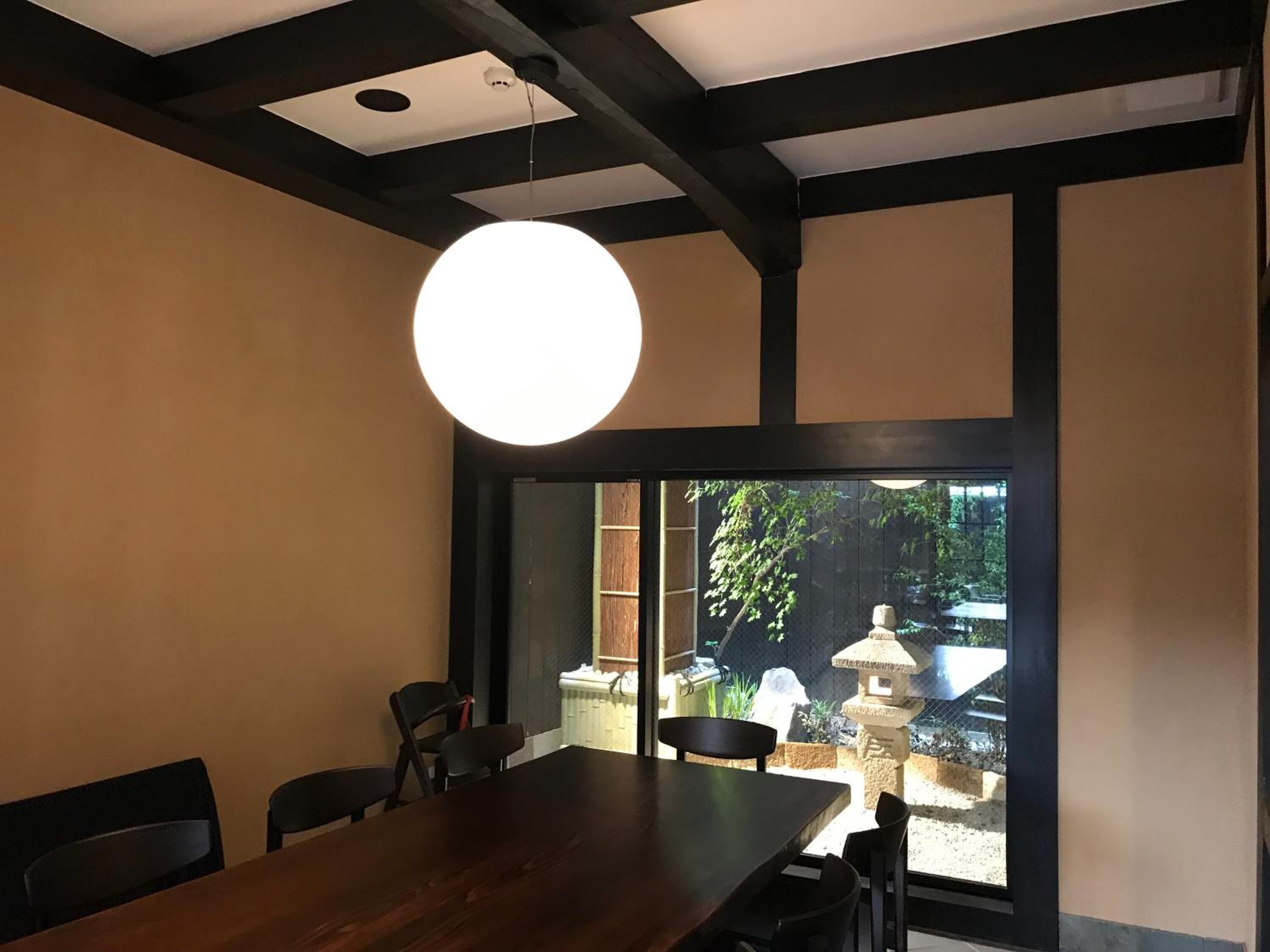 A dining area with a large table and chairs, a hanging light fixture, and a view of a garden with a stone lantern.