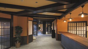 A hallway with a reception desk, wooden beams, tiled floor, and a potted plant.