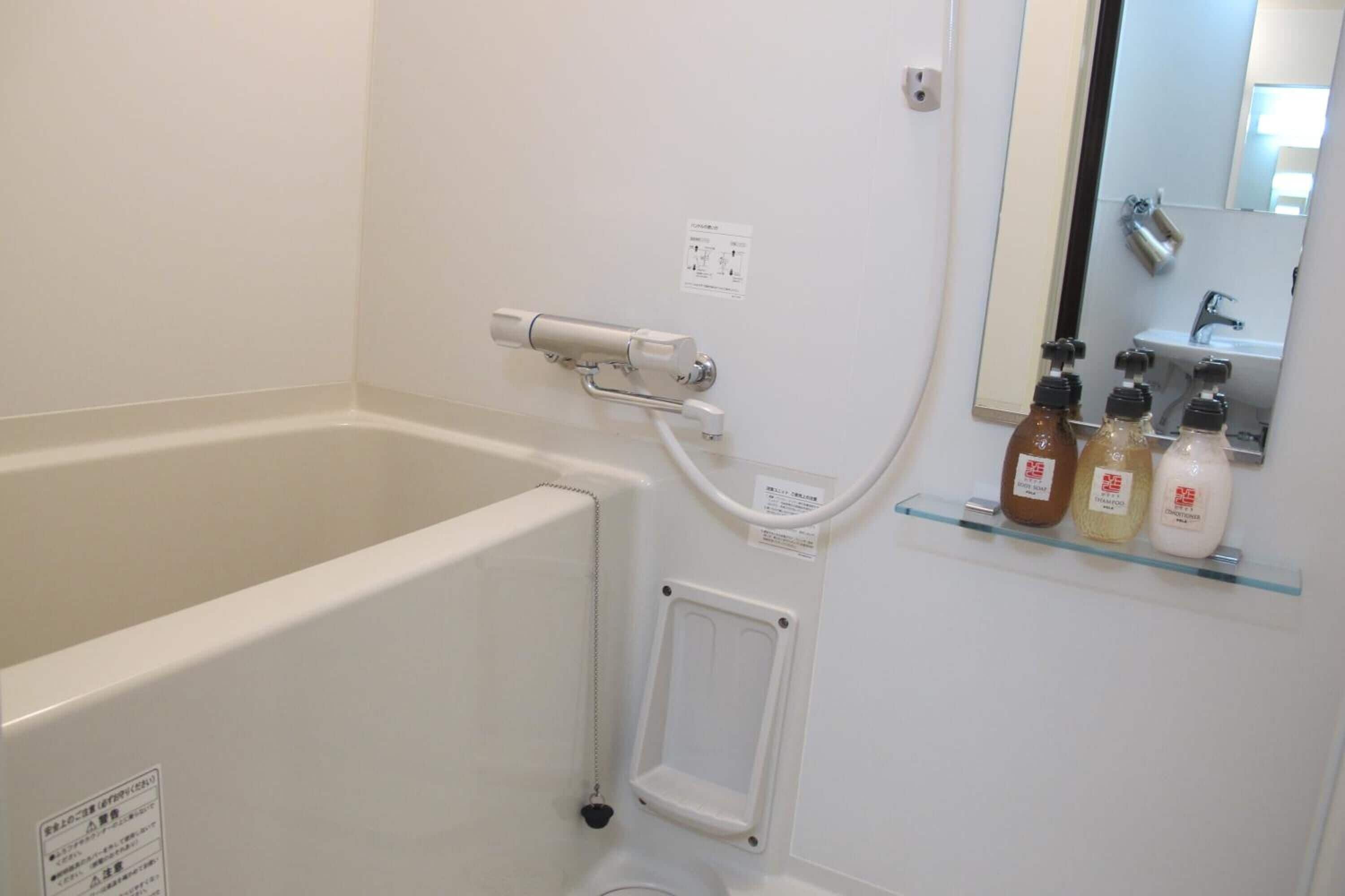 A bathroom with a bathtub, a showerhead, and a shelf with toiletries.