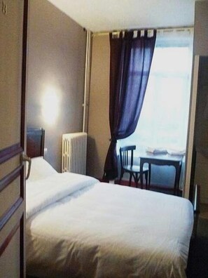 Hotellihuone, jossa on sänky, patteri, pöytä ja tuoli.