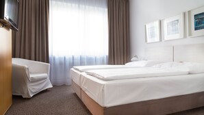 Una habitación de hotel con cama, una silla, televisor y ventana con cortinas.