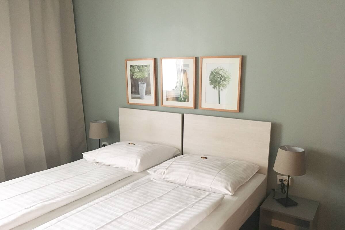 Un letto matrimoniale con biancheria bianca in una camera d'albergo. Sono presenti due comodini con lampade e tre quadri appesi alla parete sopra il letto.