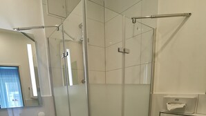 Un baño moderno con ducha acristalada, un lavabo blanco con espejo y un inodoro.